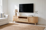 The Livia media console in Natural below a switched-off TV, in a white board-walled Cape Cod beach house with a sisal rug and a slipcovered sofa