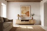The Livia media console in Natural below a large sand and terracotta painting, in a lime-washed Ibiza finca with a beamed ceiling, a jute rug and a linen sofa