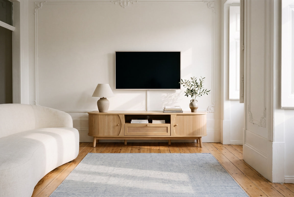 The Livia media console in Natural below a switched-off TV, in a tall Lisbon apartment with plaster cornices, pine floorboards, a blue and white rug and a curved ivory sofa