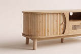 Close-up of one rounded end of the Livia console in Natural: the curved reeded pale wood door, its knob and two legs