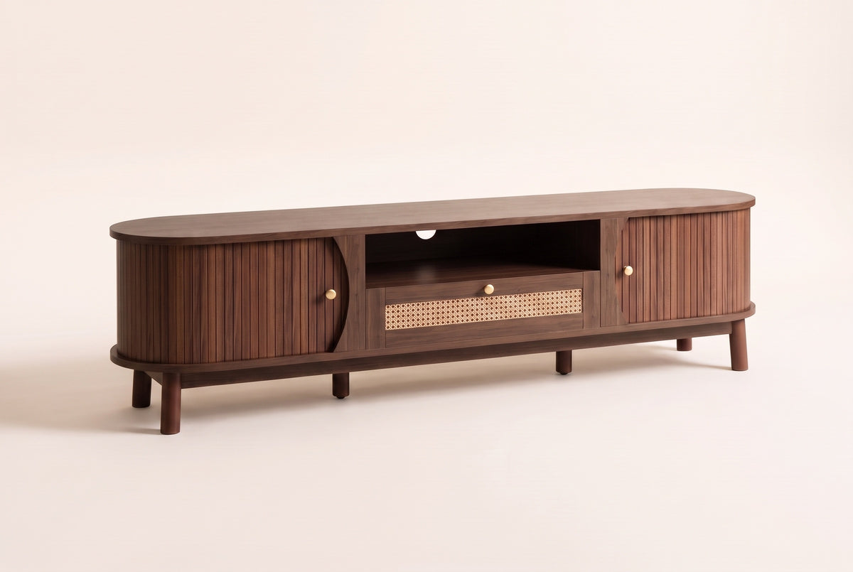 The Livia media console in Natural Walnut, front three-quarter view: rounded ends, curved reeded sliding doors, an open centre shelf and a rattan drawer on short tapered legs, on an off-white studio background