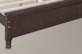 Close-up of the walnut Loreto footboard corner: square post with round bolt heads and a turned bun foot