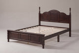 Loreto turned-post bed in walnut, three-quarter view of the bare frame on a warm grey studio backdrop