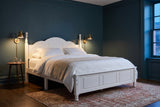 Loreto bed in white in a deep blue-green Montreal bedroom at dusk, brass wall lamps lit