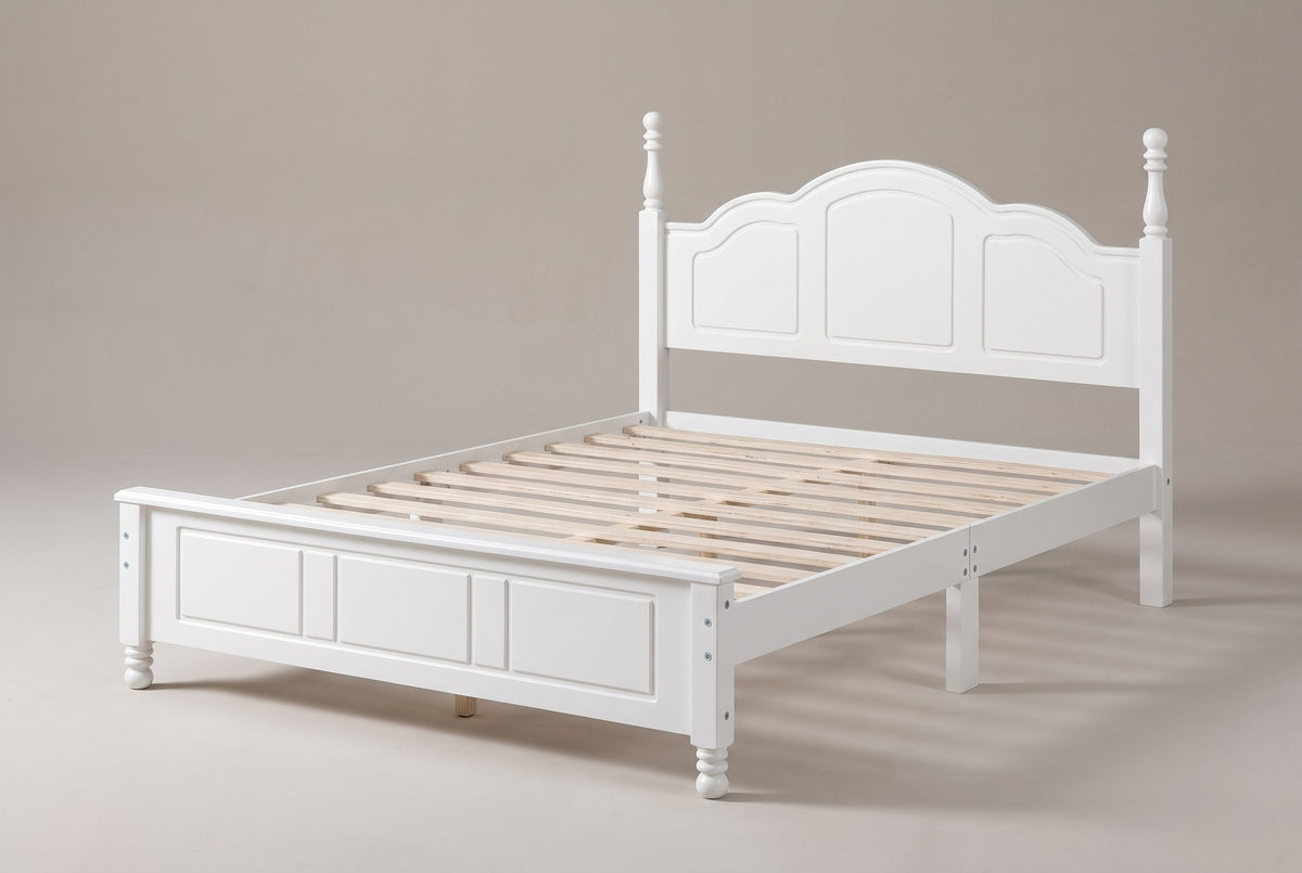 Loreto turned-post bed in white, three-quarter view of the bare frame on a warm grey studio backdrop
