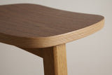 Close-up of the Lovere saddle seat: walnut veneer top, plywood layers on the edge and a square rubberwood leg