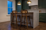 Two Lovere counter stools at a marble island under brass pendant lights in a green-cabinet Toronto kitchen at dusk