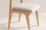 Close-up of a Lucrezia dining chair in the White Oak finish: off-white fabric seat cushion inset in the oak seat frame and tapered legs, on an off-white background