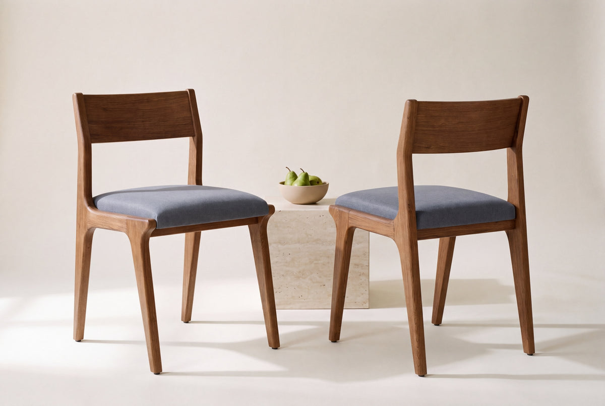 Two Lucrezia dining chairs in the Walnut finish, one seen from the front and one from behind, with pears in a bowl on a travertine block between them