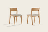 Two Lucrezia dining chairs in the White Oak finish with off-white fabric seats, one seen from the front and one from the back, on an off-white background