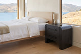 Macerata nightstand in black beside a pale oak bed in a lake house bedroom with a view of the lake and hills