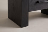 Close-up of a black slab leg standing square on the floor beside the bottom drawer and a handle post
