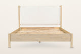 Manciano bed, raised front view on a warm white studio backdrop: the cushion headboard hanging between the two tall round hea