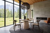 Marano round dining table in a Pemberton mountain house, with a limestone fireplace wall, a dark rattan pendant