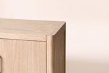 Close-up of a front top corner of the Maren cabinet in Natural: the rounded corner post and the open grain of the wood veneer