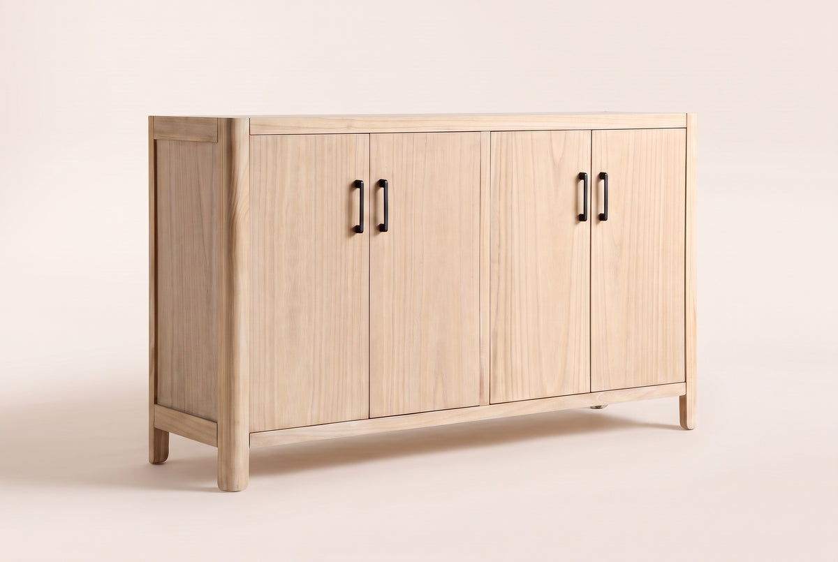 The Maren storage cabinet in Natural, front three-quarter view: four wood veneer doors with slim black handles, softly rounded corners and short solid pine legs, on an off-white studio background