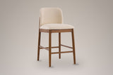 Menaggio counter stool with a rounded beige back and walnut-finish legs, three-quarter view on a warm grey studio backdrop