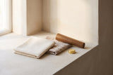 A folded swatch of the beige Menaggio fabric and a folded swatch of the textured oatmeal weave beside a walnut-finish wood le
