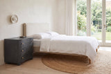 Merano nightstand in Black beside a bed with white linen in a bright Victoria bedroom with a garden door