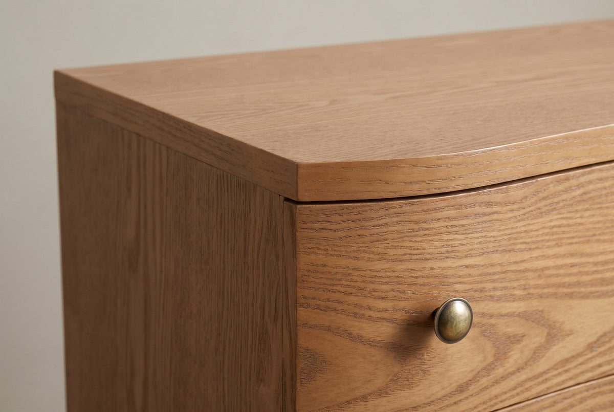Close-up of the Merano top corner: the wave-shaped top edge, the open ash grain and a round antique-brass knob