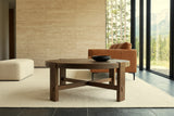 Mondavio coffee table in Smokey Chestnut seen low from the front in a Hinton mountain house, with a travertine wall