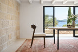 A Mondavio dining chair in side profile at a travertine table in a stone villa on Korcula