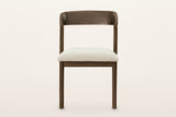 Mondavio dining chair, straight front view on a warm white studio backdrop: the curved back band above an open gap and the Iv