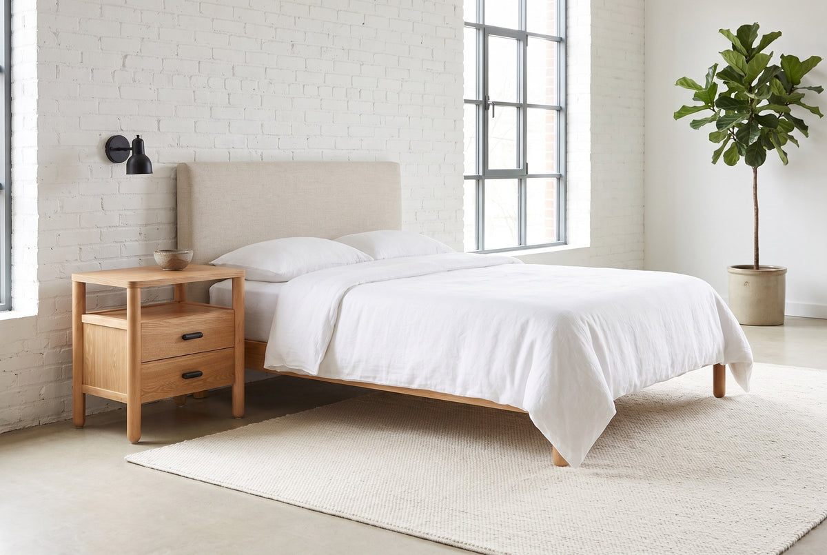 Montagnana nightstand beside a bed with white linen against a white brick wall in a bright Montreal loft