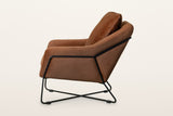 Montelupone accent chair in Rust, side view on a warm white studio backdrop: the black rod runs along the side and up the bac