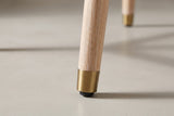 Close-up of one tapered Monteriggioni leg in brushed natural wood ending in a gold-tone foot cap with a black glide