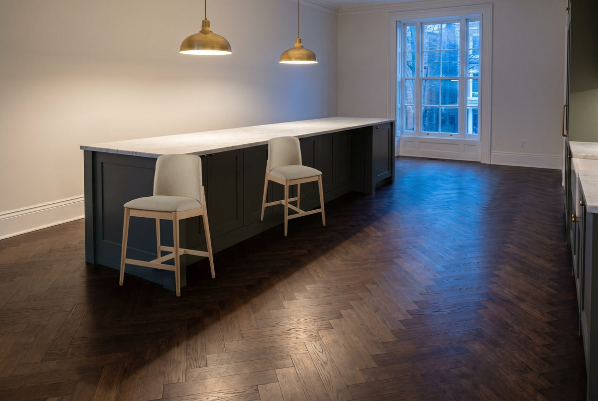 Two Monteriggioni counter stools beside a green-grey kitchen island with a marble top and brass pendant lamps in a Toronto