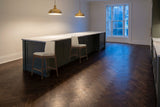 Two walnut-finish Monteriggioni counter stools beside a green-grey kitchen island with a marble top and brass pendant lamps i