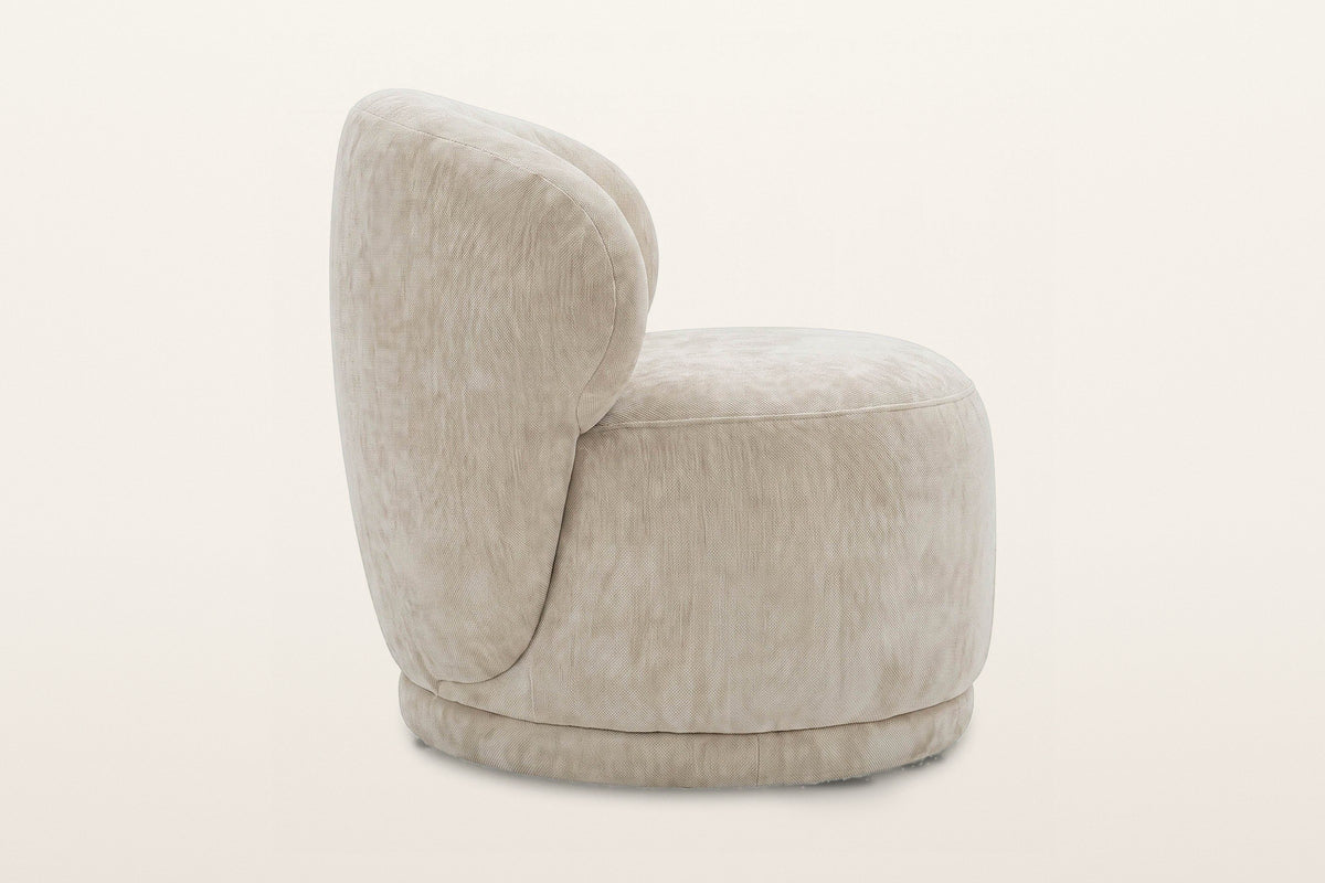 Monterubbiano accent chair in Natural velvet, side view on a warm white studio backdrop: the back wraps round and runs down t