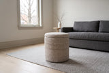 Morgex pouf in Beige on a stone-grey wool rug in a Glebe living room in Ottawa, a charcoal linen sofa behind and a bare maple through the window