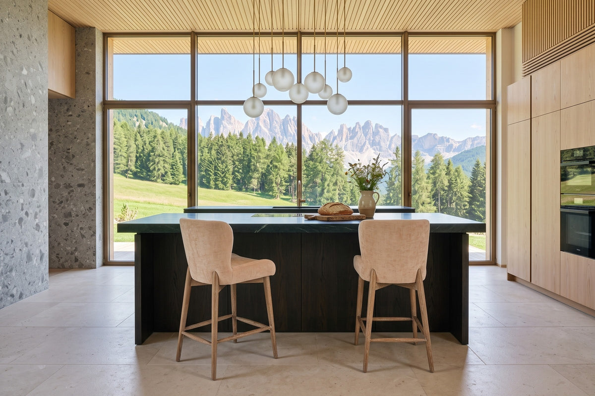 Two Morrovalle counter stools in Champagne Chenille seen from behind at a soapstone-topped smoked-oak island in a chalet in C