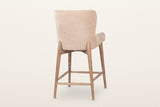 Morrovalle counter stool in Champagne Chenille from behind at an angle on a warm white studio backdrop: the rear legs rise pa