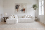 Nembo Boucle Cloud Sectional against a white wall in a Copenhagen apartment living room under an abstract painting, a paper lamp on a dark oak side table by the chaise, an olive tree at the other end and an oatmeal wool rug