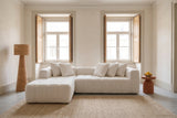 Nembo Boucle Cloud Sectional against a lime-plaster wall between two tall shuttered windows in a Lisbon living room, a rattan floor lamp by the chaise and a terracotta side table with lemons by the arm