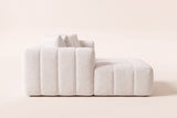 Nembo Boucle Cloud Sectional in white boucle seen from the chaise end on a warm off-white backdrop: the low channelled side sitting straight on the floor, the back and pillows rising behind