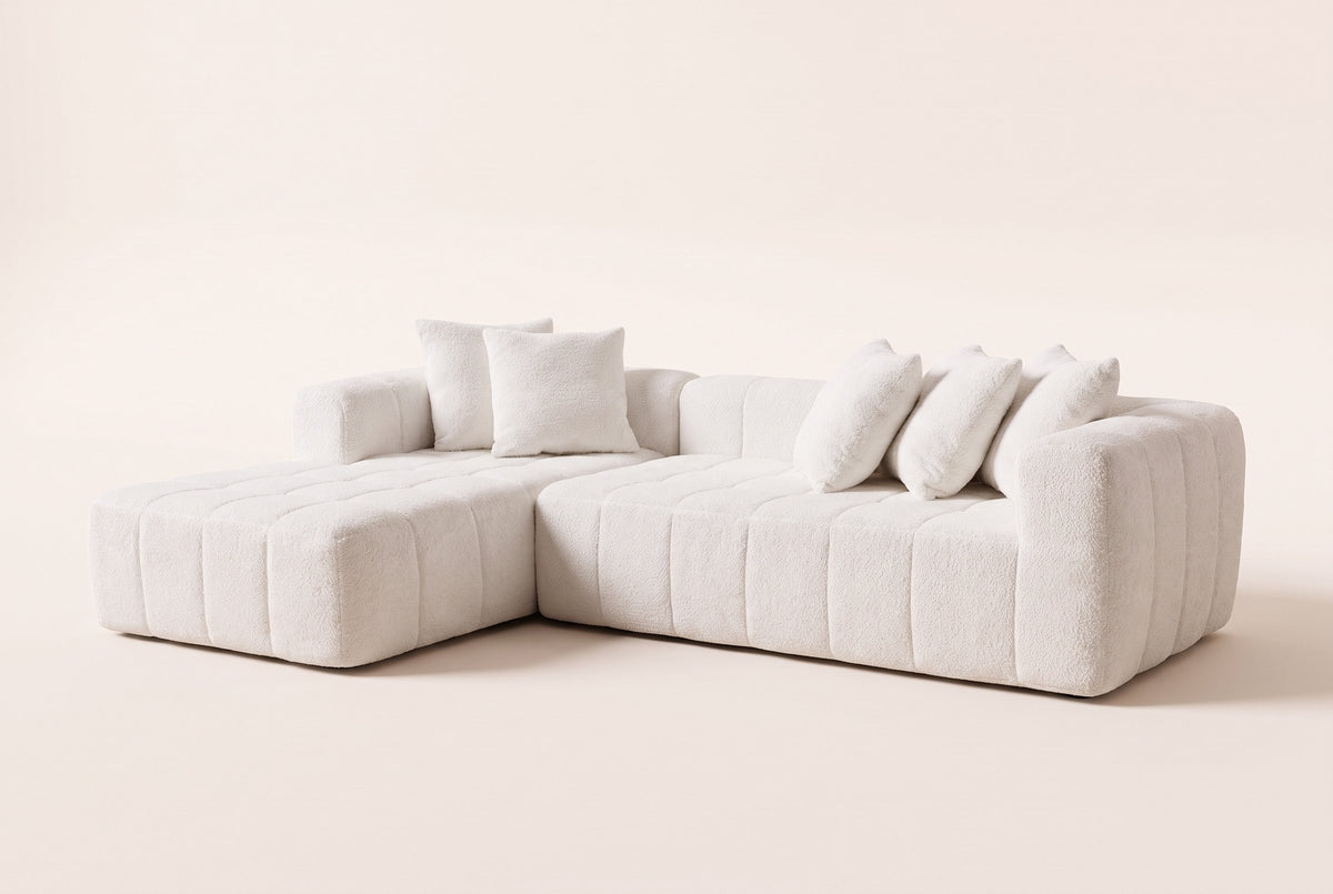 Nembo Boucle Cloud Sectional in white boucle with the chaise on the left, three-quarter view on a warm off-white backdrop: wide vertical channels, quilted square seats, one arm at the right end and no legs