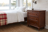 Nervi nightstand in Brown beside a bed with white linen in a whitewashed Muskoka cottage bedroom by the lake