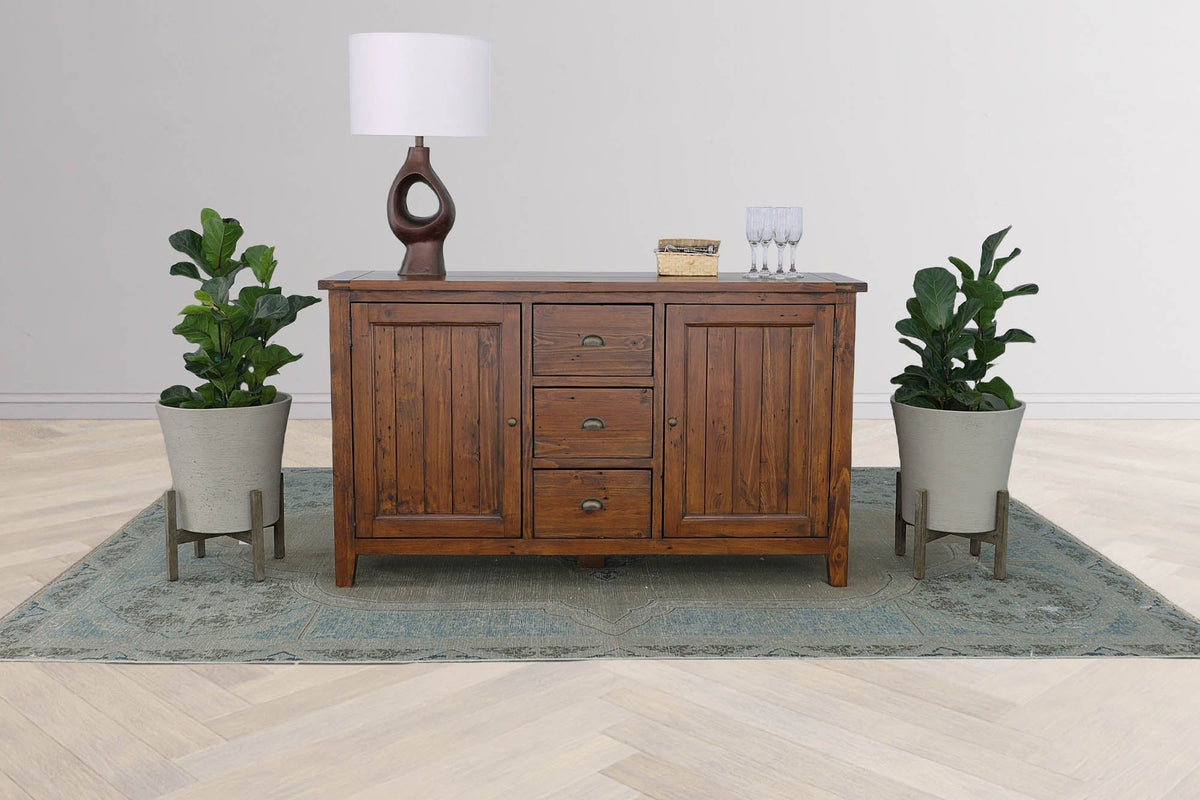 Novella sideboard styled with a table lamp between two potted plants on a blue rug