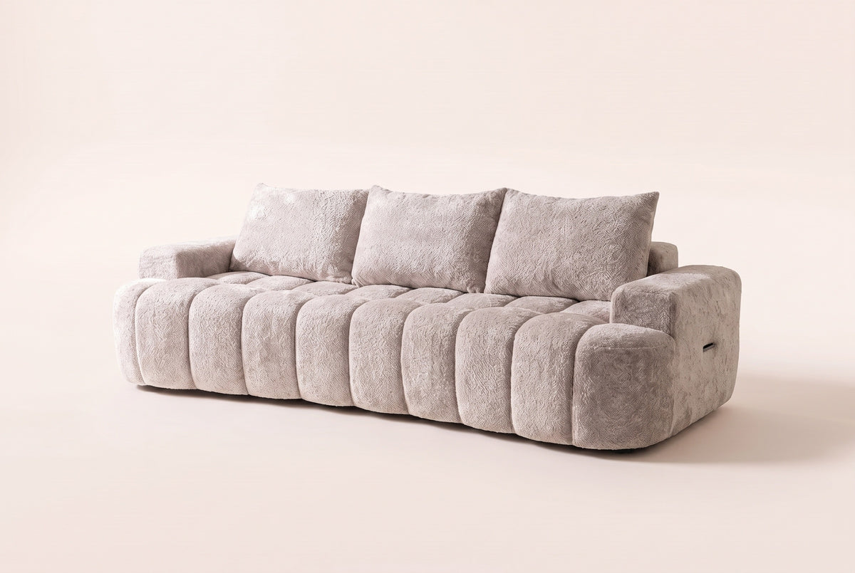 The Nuvola sofa in Camel, front three-quarter view: a long, low channel-tufted boucle sofa with a softly curved front, low arms and three back pillows, on an off-white studio background