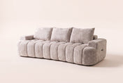 The Nuvola sofa in Camel, front three-quarter view: a long, low channel-tufted boucle sofa with a softly curved front, low arms and three back pillows, on an off-white studio background