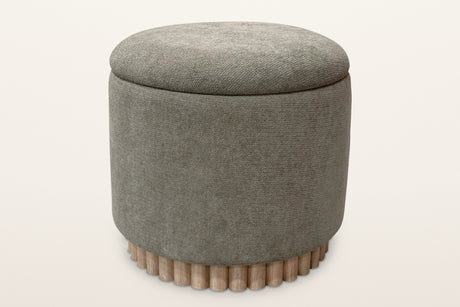 Nyla round storage ottoman in moss green chenille on a reeded light-wood base, seen from slightly above on a warm white studio backdrop