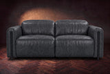 The Octavia loveseat in Aged Slate distressed full leather on a dark herringbone floor, seen from the front, headrests down. Shown in Aged Slate, Loveseat.