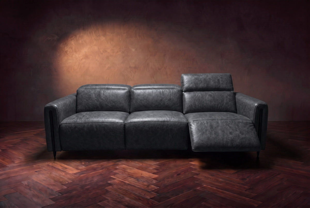 The Octavia 3 seat in Aged Slate distressed full leather on a dark herringbone floor, seen from the front, the right recliner open and its headrest raised. Shown in Aged Slate, 3 seat.
