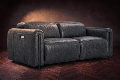 The Octavia loveseat in Aged Slate distressed full leather on a dark herringbone floor, headrests down and footrests closed. Shown in Aged Slate, Loveseat.