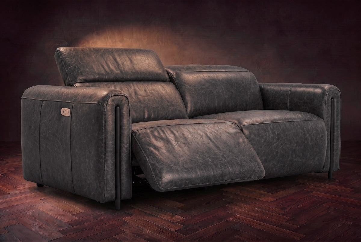 The Octavia loveseat in Aged Slate distressed full leather on a dark herringbone floor, the left recliner open and its headrest raised. Shown in Aged Slate, Loveseat.