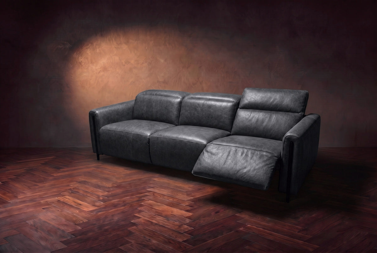 The Octavia 3 seat in Aged Slate distressed full leather on a dark herringbone floor, seen from the right, the right recliner open and its headrest raised. Shown in Aged Slate, 3 seat.